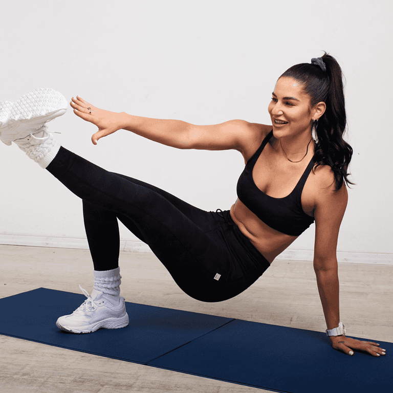 A woman in athletic attire performs a side plank with leg lift on a blue exercise mat. She extends her right arm and left leg, smiling as she balances on her right hand and left foot. This routine is all about mastering balance and strength together.