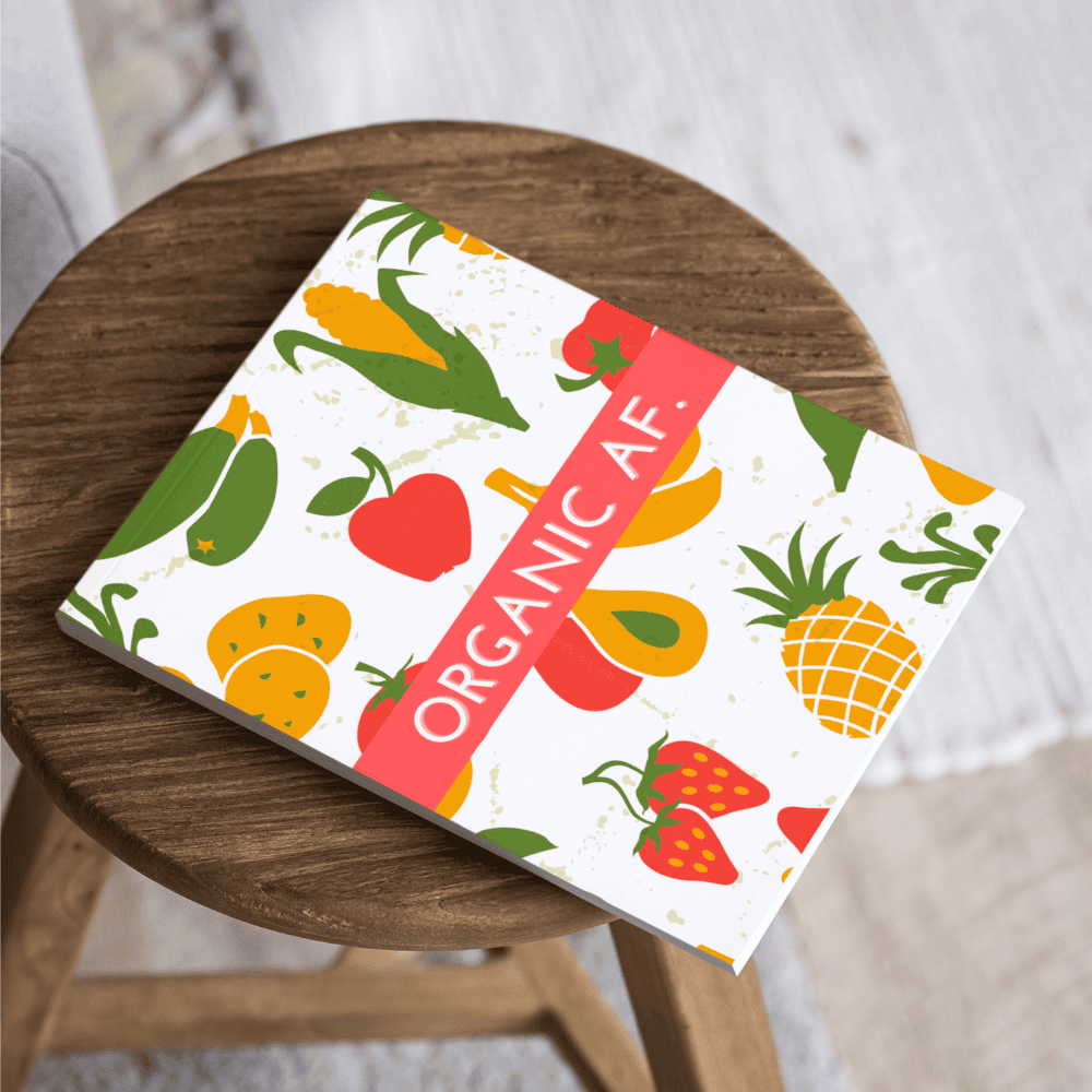 A book titled "ORGANIC AF" with illustrated fruits and vegetables on the cover, resting on a round wooden stool in a cozy bookstore.
